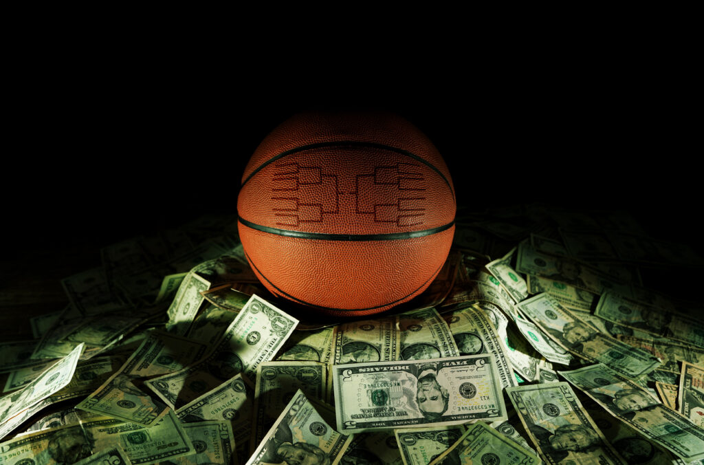 Basketball with a tournament bracket design sitting on a pile of cash, symbolizing March Madness betting and sportsbook revenue.